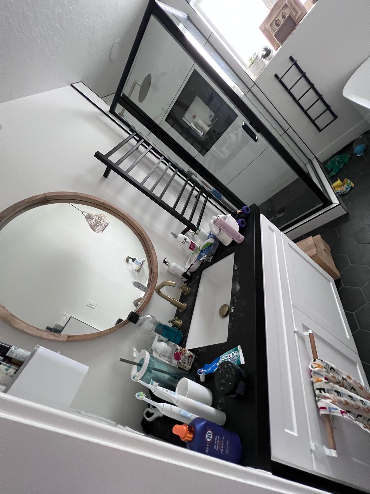 Residential bathroom before deep cleaning with cluttered vanity and floor items.