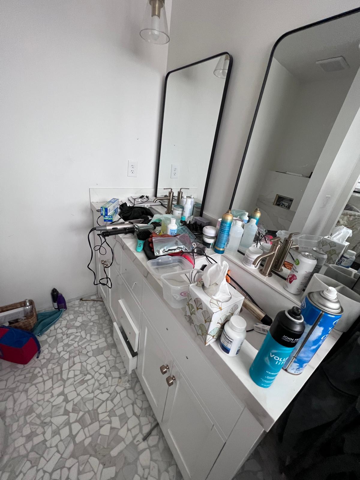 Bathroom sink and vanity before cleaning with products and clutter on the counter.